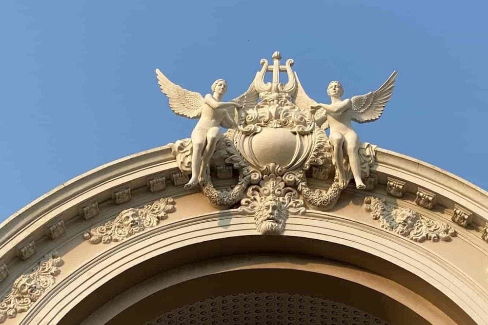 A detailed view of the Ho Chi Minh City Opera House façade, showcasing its ornate French colonial sculptures, including two winged figures holding a lyre, symbolizing art and music